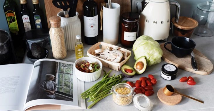 Various colorful healthy food and vegetables locating on countertop next to many different utensils and white kettle during cooking in stylish kitchen