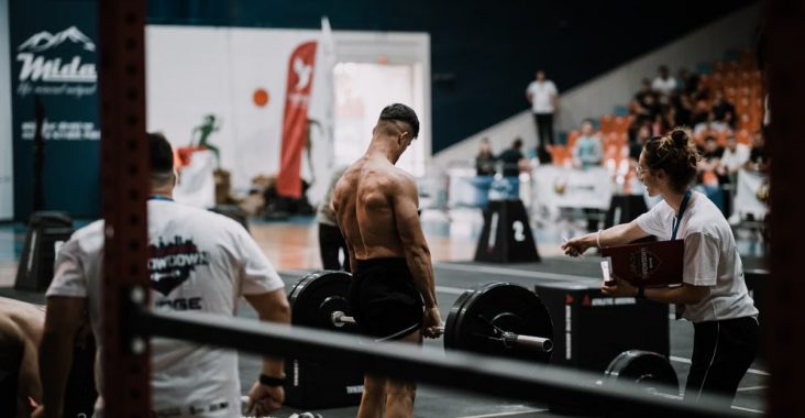 A weightlifting athlete prepares for a lift during a competition with judges observing.